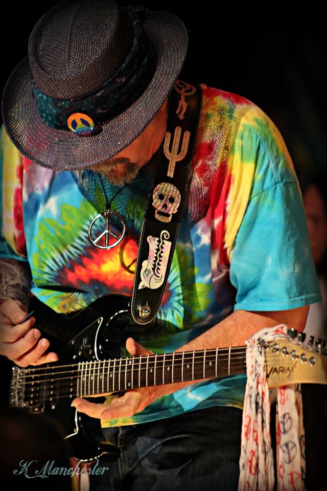 Musician wearing a tie dye shirt and fedora playing a Variax electric guitar