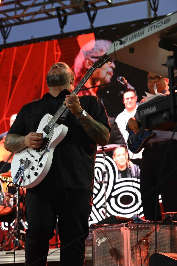 Person playing guitar on stage with a band in the background