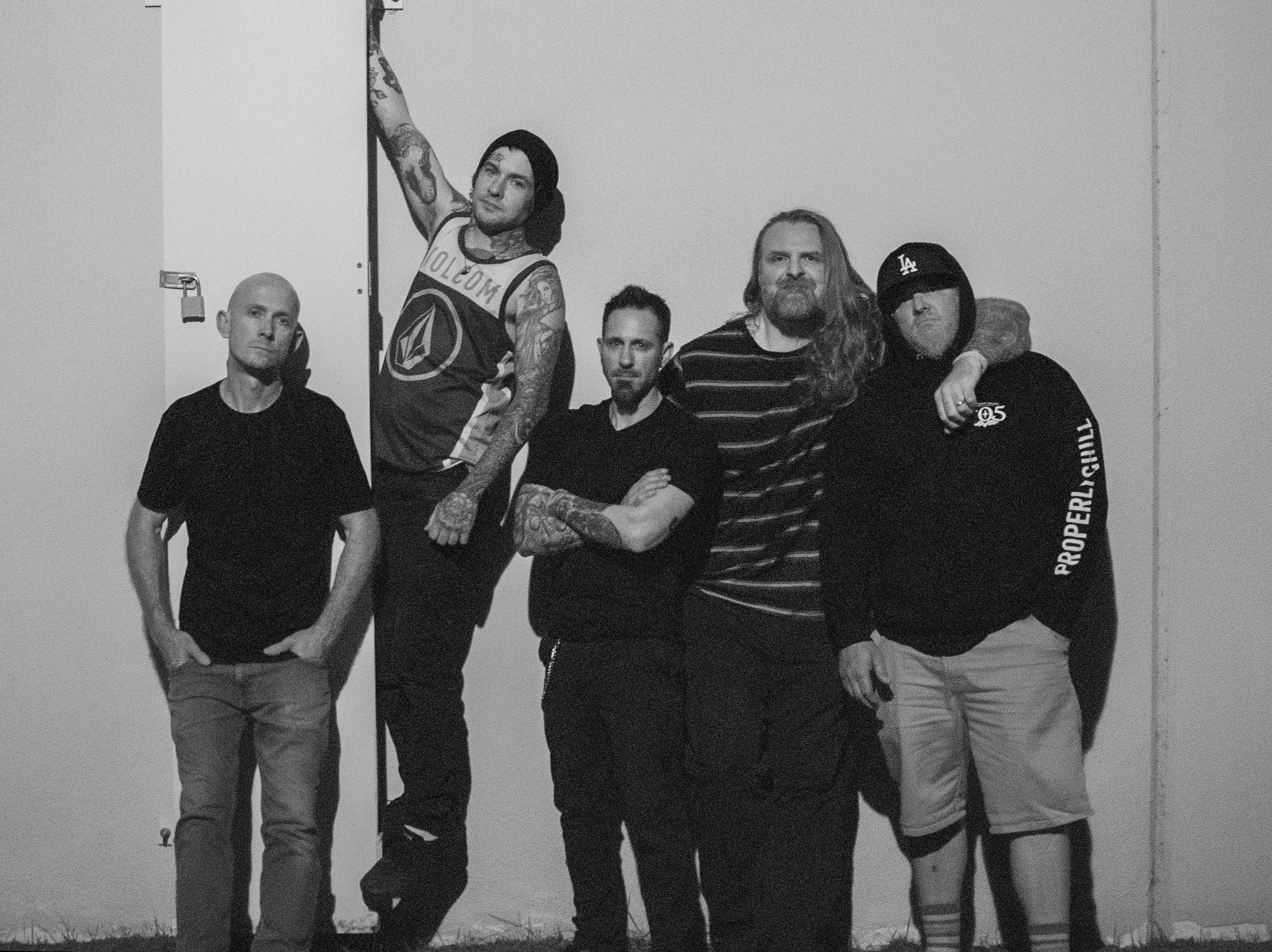Five men standing in a row against a plain wall