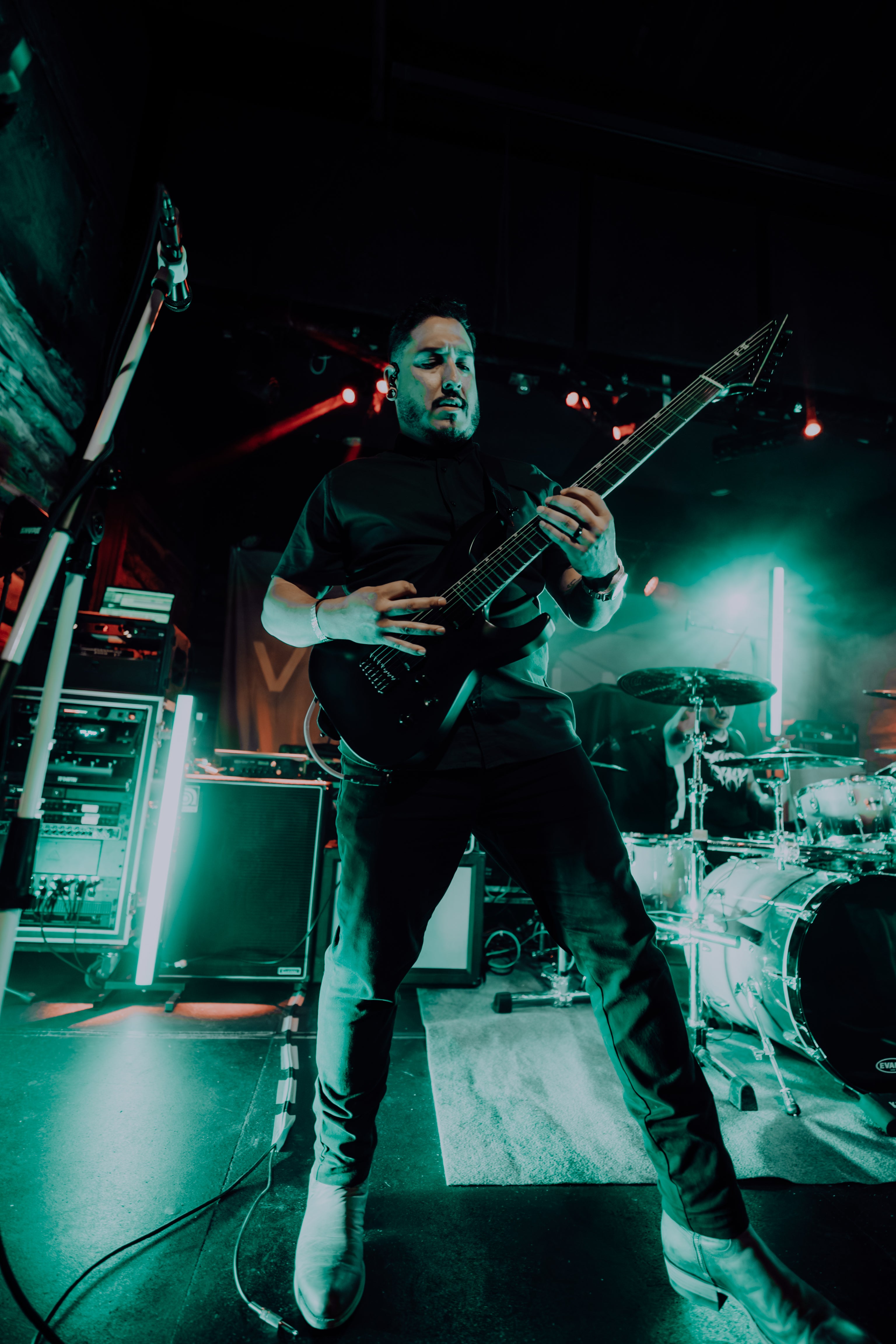 Guitarist playing a black electric guitar on stage under green lighting