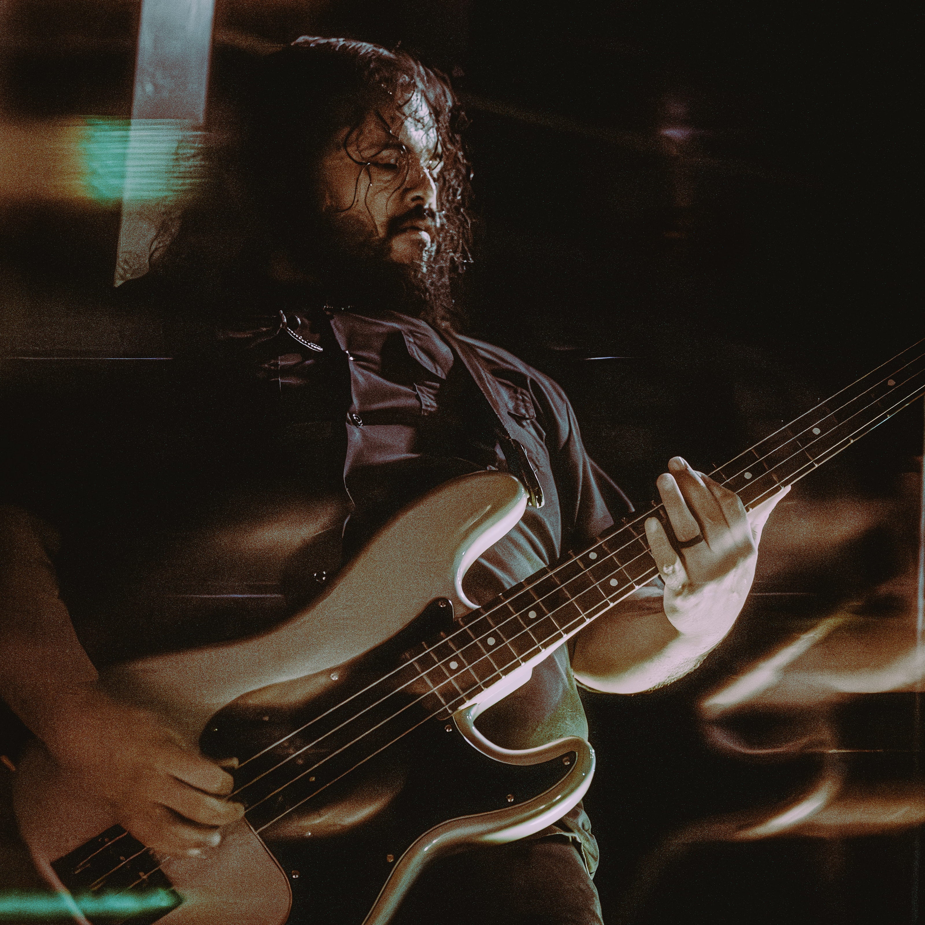 Bearded musician playing a bass guitar on stage under dim lighting