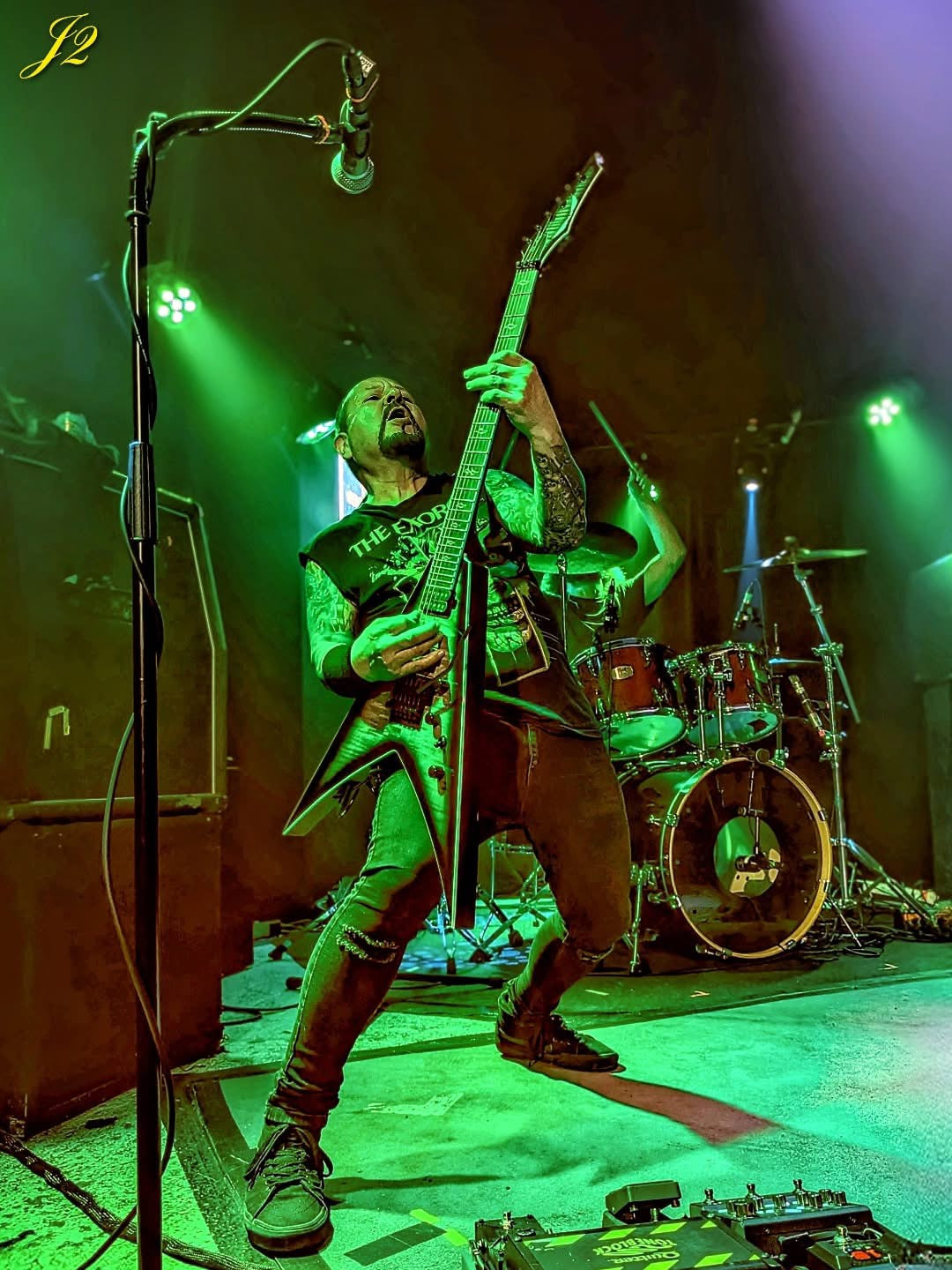 Guitarist playing a V-shaped electric guitar on stage under green lighting