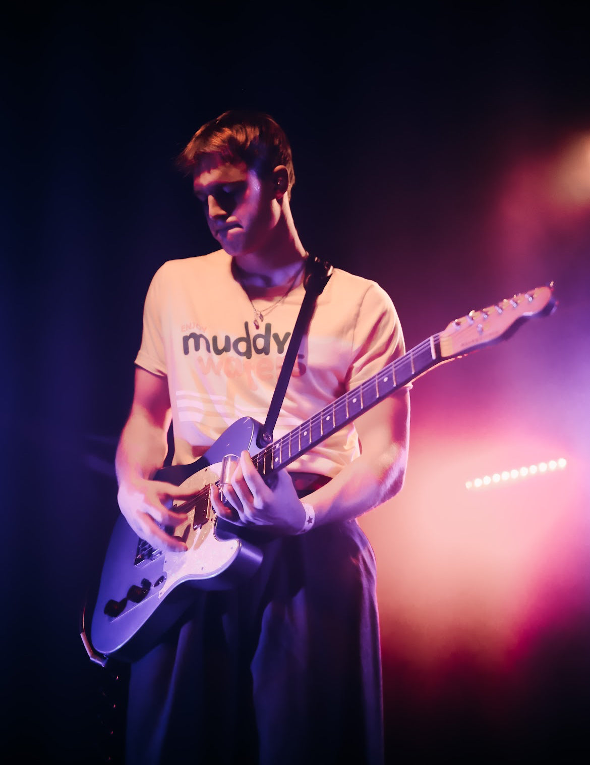 Person playing guitar with 'muddv' shirt on a dark background