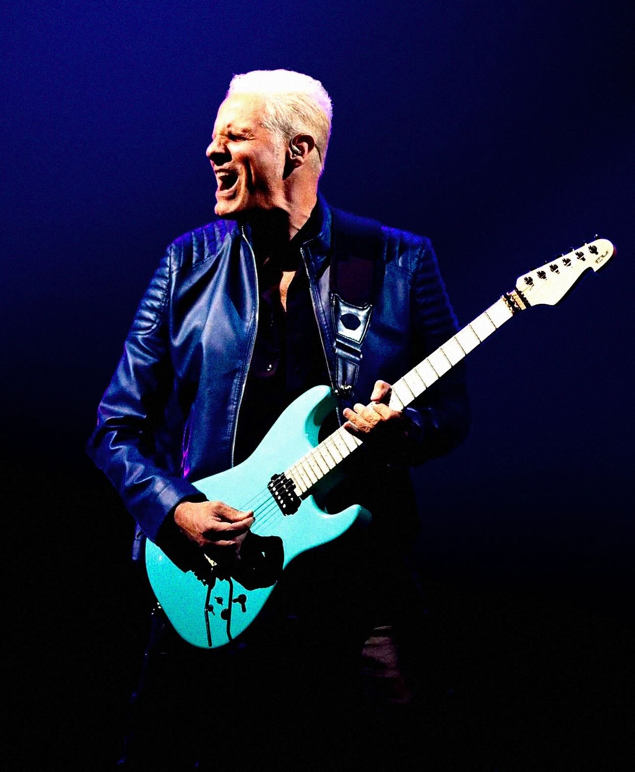 Person playing a blue electric guitar against a dark background
