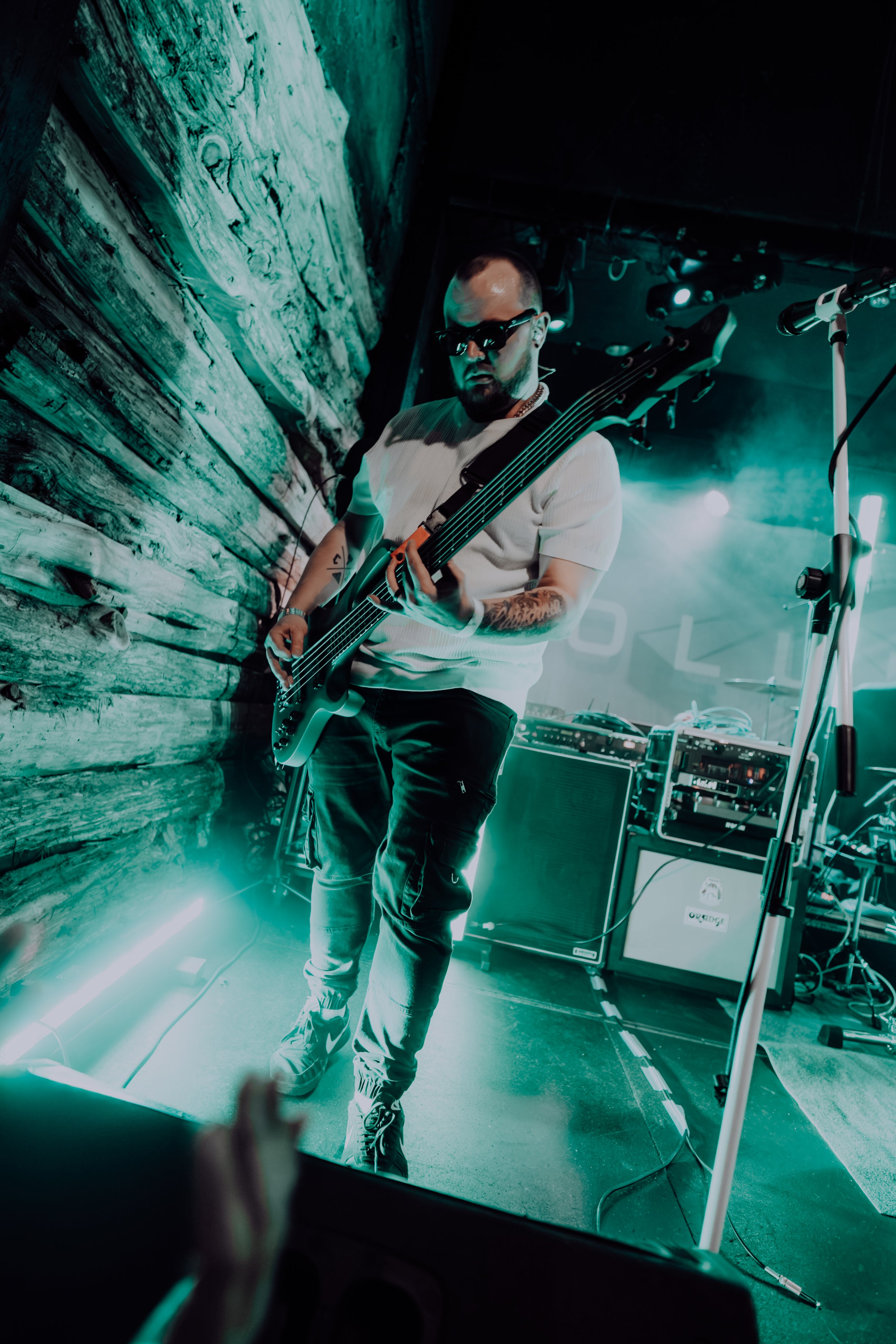 Musician playing bass guitar on stage under green lighting